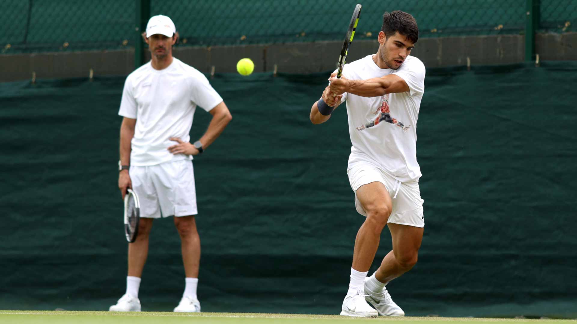 <a href='https://www.atptour.com/en/players/carlos-alcaraz/a0e2/overview'>Carlos Alcaraz</a> practises at <a href='https://www.atptour.com/en/tournaments/wimbledon/540/overview'>Wimbledon</a> while coach <a href='https://www.atptour.com/en/players/juan-carlos-ferrero/f316/overview'>Juan Carlos Ferrero</a> looks on.