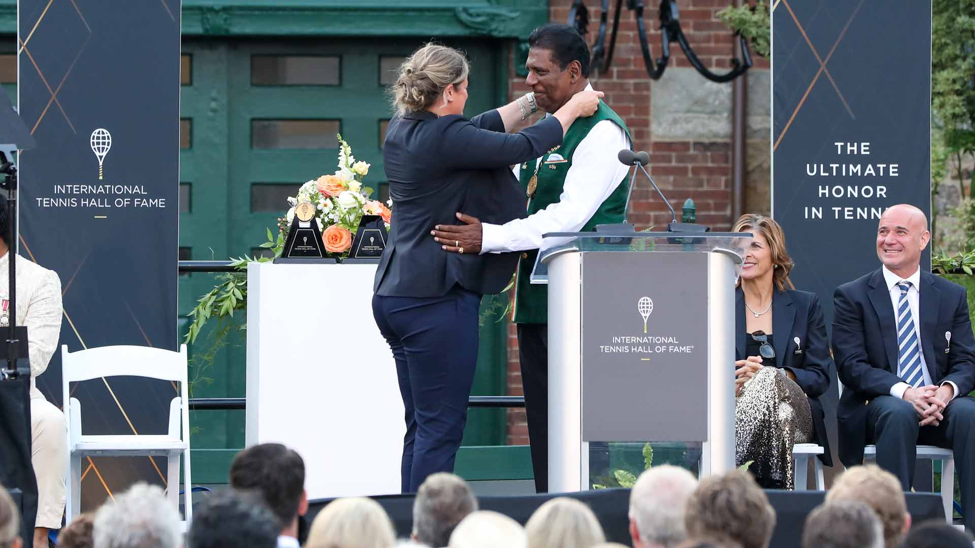 International Tennis Hall of Fame Honourary President Kim Clijsters presents <a href='https://www.atptour.com/en/players/vijay-amritraj/a022/overview'>Vijay Amritraj</a> with a medal upon his induction Saturday in Newport.