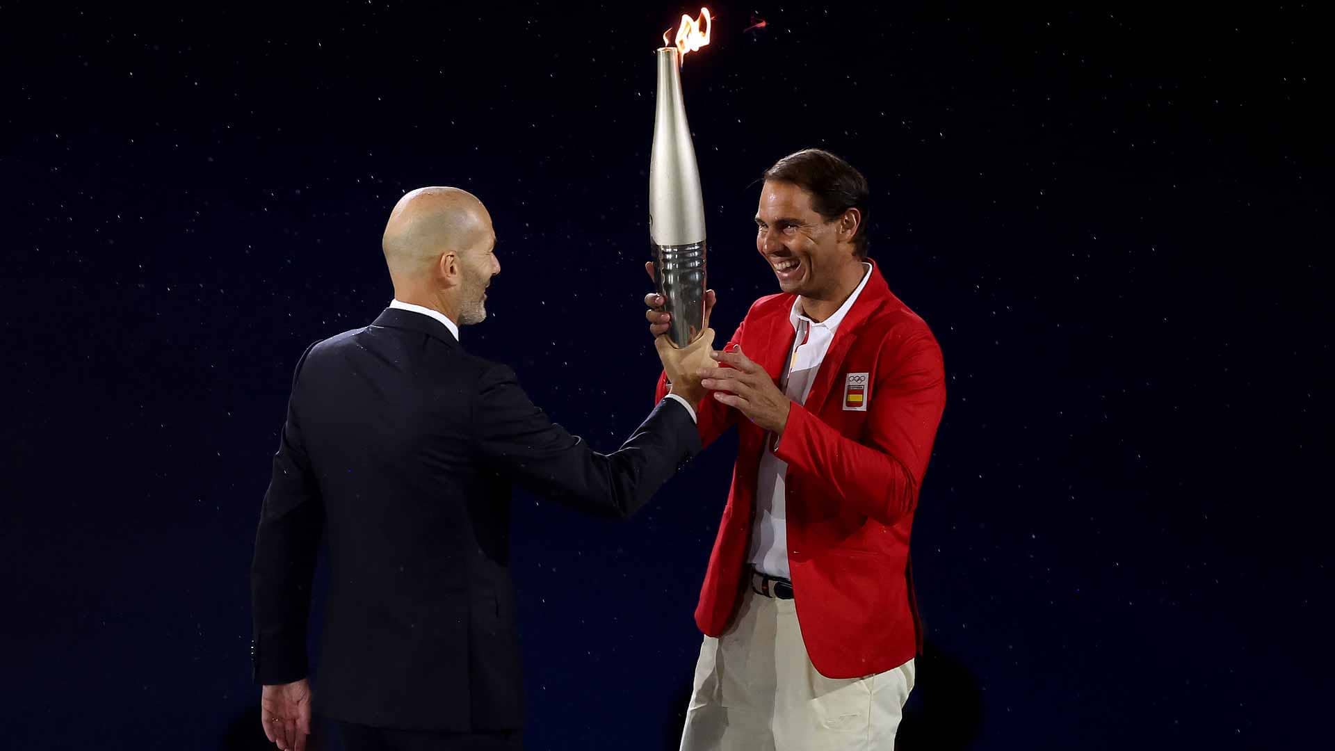 Zinedine Zidane hands the Olympic Torch to <a href='https://www.atptour.com/en/players/rafael-nadal/n409/overview'>Rafael Nadal</a> during Friday evening's Opening Ceremony in Paris.